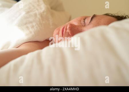 Une photo en gros plan d'une jeune femme reposant paisiblement dans son lit, la tête sur un oreiller, montrant des taches de rousseur sur sa joue et une expression sereine. Banque D'Images