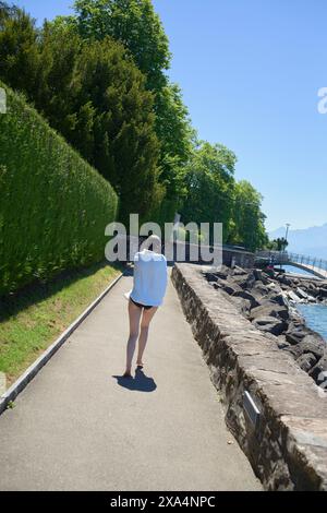 Une personne marche le long d'un chemin pavé par un lac avec une végétation luxuriante et un ciel clair en arrière-plan. Banque D'Images
