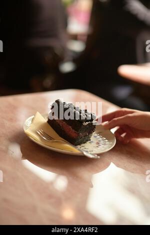 Tranche de gâteau au chocolat orné de baies sur une assiette avec un doigt humain le touchant doucement. Banque D'Images