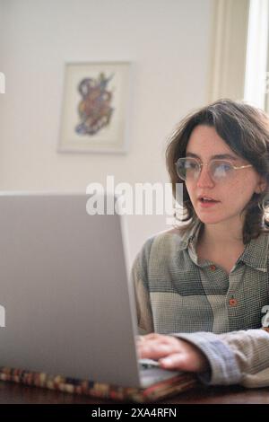 Jeune adulte travaillant intensément sur un ordinateur portable dans un cadre domestique Banque D'Images