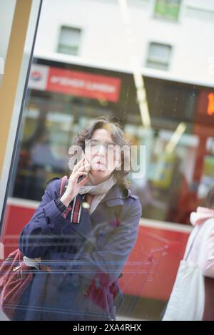 Femme espiègle sortant sa langue lors d'un appel téléphonique à travers un reflet de verre. Banque D'Images