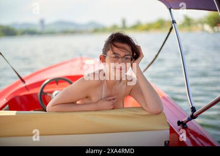 Jeune femme profitant d'un moment de détente sur un bateau rouge au bord du lac. Banque D'Images