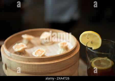 Boulettes cuites à la vapeur dans un cuiseur vapeur en bambou associées à un verre rafraîchissant de thé glacé garni de citron. Banque D'Images