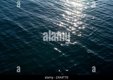 Lumière du soleil se reflétant sur la surface tranquille de l'eau bleue avec de douces ondulations. Banque D'Images