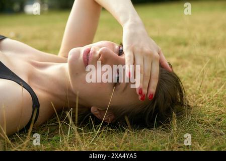 Jeune femme aux ongles rouges couchée sur l'herbe, couvrant ses yeux avec sa main. Banque D'Images