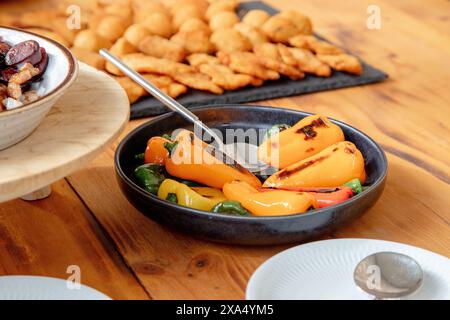 Un assortiment de poivrons grillés, servis dans un bol noir, ajoute une option colorée et saine à la propagation des collations frites et des viandes Banque D'Images