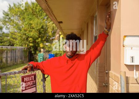 Un jeune homme portant un sweat à capuche rouge se penche sur une balustrade métallique à l'ombre d'un bâtiment avec un panneau « propriété privée non intrusive ». Banque D'Images
