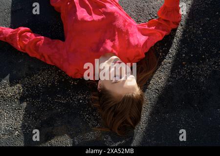 Une femme dans une blouse rouge vif se trouve sur le sol avec ses cheveux étendus, capturés d'en haut. Banque D'Images