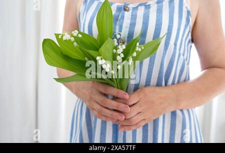 Une femme dans une robe rayée bleue tenant un bouquet de lys frais de la vallée. Parfait pour illustrer les humeurs printanières et la beauté naturelle. Banque D'Images