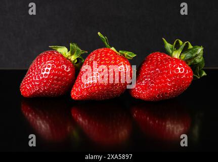 Un gros plan de trois fraises fraîches sur une table sur un fond noir Banque D'Images