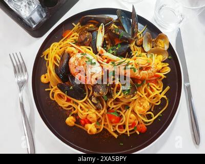 Spaghetti de pâtes italiennes classiques aux fruits de mer avec palourdes, moules, crevettes, cocktail de fruits de mer sur une table sombre, gros plan. Pâtes spaghetti avec sauce marinara. Banque D'Images