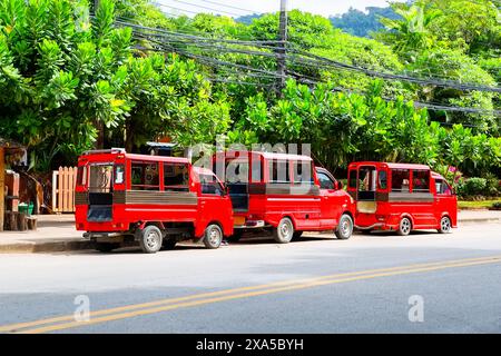 Trois taxis traditionnels thaïlandais en tuk tuk rouge (songthaew) à Krabi, Thaïlande. Taxi tuk-tuk rouge garé le long de la route en Thaïlande. Banque D'Images