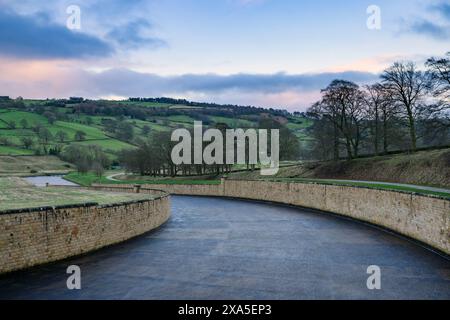 Chute d'eau, descente en pente douce, murs de soutènement en pierre, campagne pittoresque et coucher de soleil en soirée - réservoir Swinsty, Angleterre, Royaume-Uni. Banque D'Images