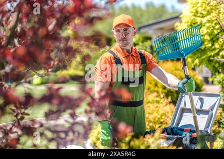 Un jardinier caucasien travaillant dans le jardin verdoyant et le nettoyant des feuilles et de l'herbe Banque D'Images