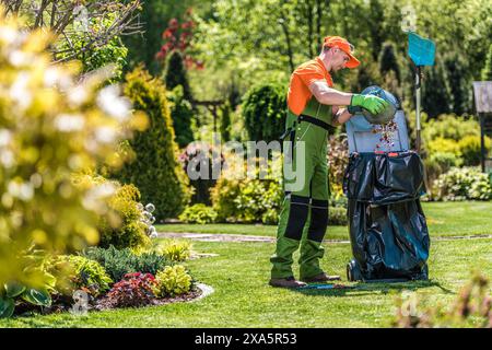 Un jardinier caucasien travaillant dans le jardin verdoyant et le nettoyant des feuilles et de l'herbe Banque D'Images