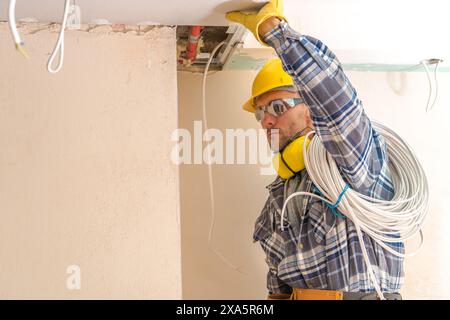 Un électricien caucasien installant des câbles pendant les travaux de construction Banque D'Images