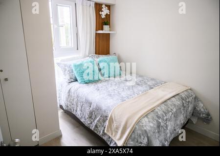 Chambre lumineuse et aérée avec un lit soigneusement fait avec des oreillers décoratifs et une fenêtre Banque D'Images