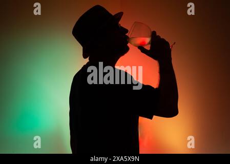 Portrait d'un homme non identifié en silhouette buvant du liquide d'un verre transparent. Isolé sur fond coloré. Banque D'Images