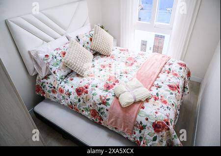 Cette chambre lumineuse et accueillante comprend un lit avec une couette à motifs floraux colorés et des oreillers décoratifs Banque D'Images