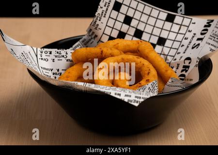 Un bol de rondelles d'oignon croustillantes enveloppées dans du journal sur une table en bois rustique Banque D'Images
