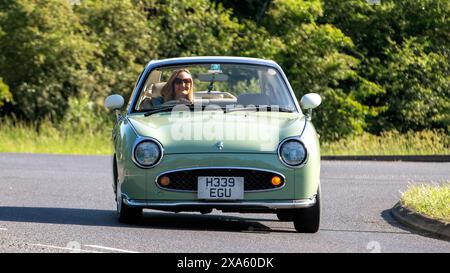 Stony Stratford, Royaume-Uni - 2 juin 2024 : 1991 voiture classique Nissan Figaro verte conduisant sur une route de campagne britannique Banque D'Images