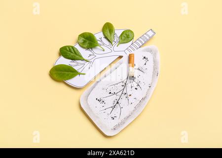 Poumons en papier avec cigarette et feuilles vertes sur fond jaune Banque D'Images