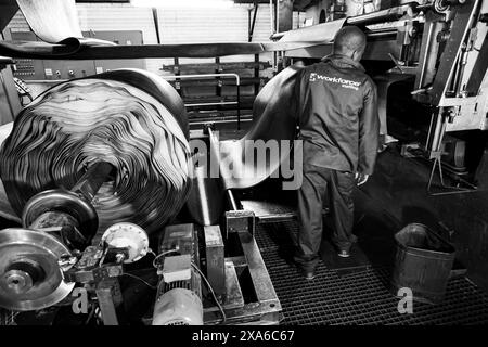Un ouvrier d'usine africain inspectant le rouleau en caoutchouc sur la machine de bande transporteuse dans l'usine de Johannesburg Banque D'Images
