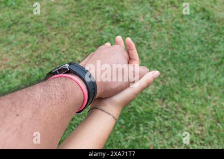 gros plan des mains entrelacées d'un couple homme-femme. L'homme porte une montre noire et la femme porte une montre. Vous pouvez voir le ciel an Banque D'Images