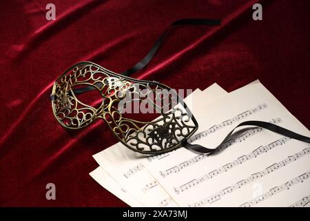 Masque facial élégant et feuilles de musique sur tissu rouge. Représentation théâtrale Banque D'Images