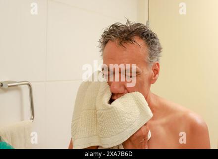 Homme mûr séchant son visage dans la salle de bain avec une serviette après la douche Banque D'Images