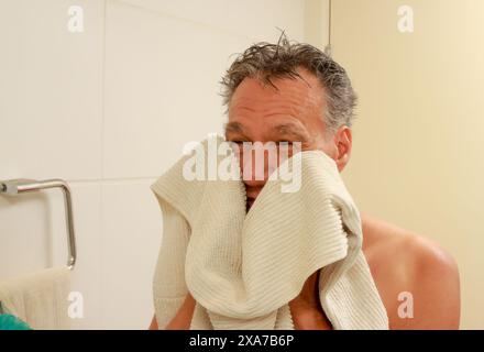 Homme mûr séchant son visage dans la salle de bain avec une serviette après la douche Banque D'Images