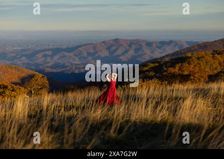 Une femme dans une robe rouge regarde l'horizon sur un champ de montagne Banque D'Images