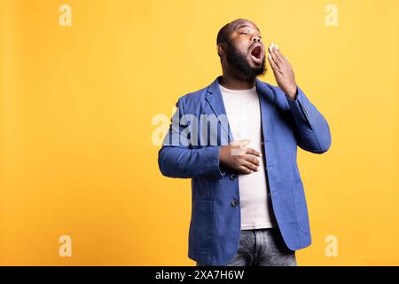 Homme afro-américain se sentant épuisé et bâillant, couvrant sa bouche, isolé sur fond de studio. BIPOC personne somnolente pendant la matinée, se réveille trop tôt, montrant de la somnolence Banque D'Images