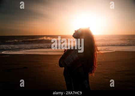 Une femme en tenue sombre illuminée par la lumière du soleil au-dessus de sa tête Banque D'Images
