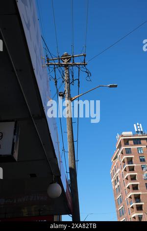 Un poteau électrique en bois avec des lignes électriques et un lampadaire s'élève au-dessus d'un auvent dans un ciel bleu clair sur King Street, Newtown, Sydney Banque D'Images
