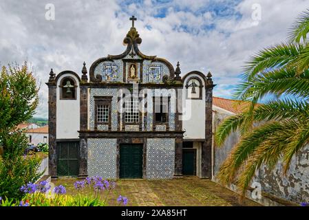 Couvent historique de l'église de Caloura avec motif typique de tuiles, façade bleue et blanche et symboles religieux. Vue extérieure avec ciel nuageux et jardin Banque D'Images