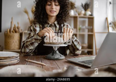 Femme créant des poteries dans son home studio avec ordinateur portable Banque D'Images