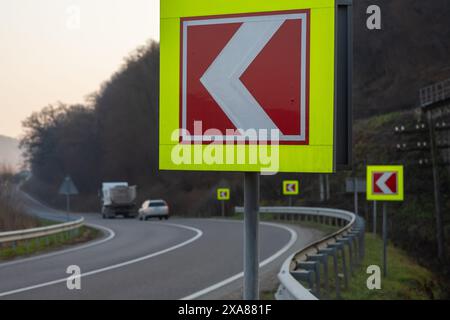 Route asphaltée avec des panneaux de signalisation lumineux in situ du virage à gauche serré. Banque D'Images