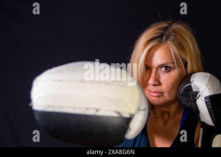 portrait femme blonde adulte posant avec des gants de boxe sur un fond noir Banque D'Images