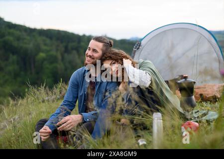 Couple de voyageurs passant du temps à l'extérieur, dormant dans un abri de tente. Jeune touriste assis dans la nature, se reposer, profiter du coucher du soleil. Vacances d'été en Banque D'Images