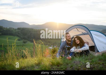 Couple de voyageurs passant du temps à l'extérieur, dormant dans un abri de tente. Jeune touriste assis dans la nature, se reposer, profiter du coucher du soleil. Vacances d'été en Banque D'Images