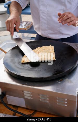 Un homme prépare un dessert sur une poêle noire. Le dessert est une crêpe, et l'homme utilise une spatule pour étaler une sauce dessus. La scène est casual et rel Banque D'Images