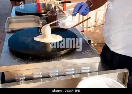 Un homme fait des crêpes sur une plaque chauffante. Une femme tient un bébé dans une poussette Banque D'Images