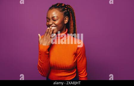 Femme noire élégante dans sa vingtaine avec des tresses bicolores vibrantes, debout sur un fond violet joyeux. Banque D'Images