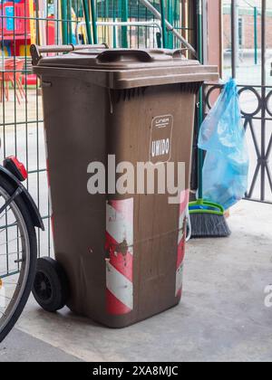 Cremona, Italie - 27 mai 2024 Grande poubelle à roulettes brune avec un couvercle fermé, debout sur une surface dure. Le bac présente des signes d'usure. Banque D'Images