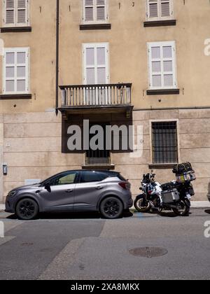 Cremona, Italie - 27 mai 2024 moto et voiture sont garées dans une rue vide dans une petite ville italienne, profitant du soleil d'été. Banque D'Images