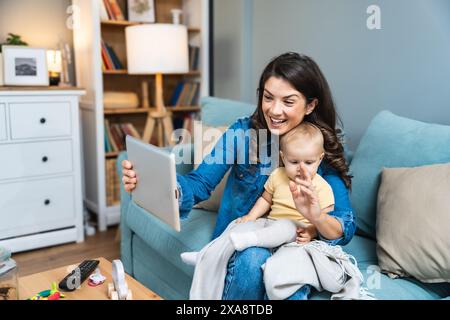 Maman de famille heureuse et fille enfant utilisant la tablette numérique assise sur le canapé, mère parent souriante avec la fille enfant tenant l'ordinateur pc regardant l'écran do Banque D'Images