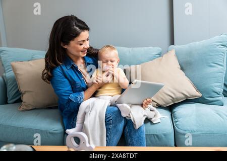 Maman de famille heureuse et fille enfant utilisant la tablette numérique assise sur le canapé, mère parent souriante avec la fille enfant tenant l'ordinateur pc regardant l'écran do Banque D'Images