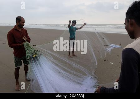 5 juin 2024, Cox's Bazar, Chittagong, Bangladesh : des pêcheurs préparent des filets de pêche pour attraper du poisson sur la plage de la mer de Cox's Bazar, Bangladesh. Le gagne-pain de la communauté des pêcheurs ici dépend largement de la pêche. Avec chaque nœud et ajustement, ils honorent une tradition intemporelle de subsistance qui s'harmonise avec les rythmes du monde naturel. Cox's Bazar, la plus longue plage marine naturelle du monde, s'étend sur plus de 120 kilomètres le long de la côte sud-est du Bangladesh. Réputée pour son sable doré, ses couchers de soleil vibrants et ses vagues, elle attire des millions de touristes chaque année. (Crédit image : © Joy Banque D'Images