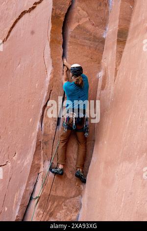 Un grimpeur en tête utilisant la technique du brouillage pour se soutenir lors d'une ascension à Wall Street, près de Moab, Utah. Coincer, c'est forcer votre main à entrer Banque D'Images